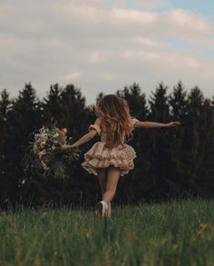 a girl in a dress is running through the grass with her arms outstretched and holding flowers