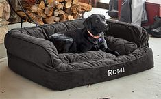 a black dog is sitting in his bed on the floor next to some firewood