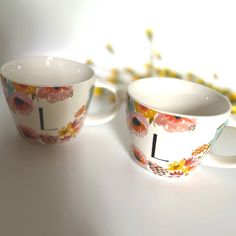 two coffee cups sitting next to each other on top of a white table with yellow flowers