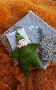 a green stuffed toy laying on top of a bed next to pillows and a pillow