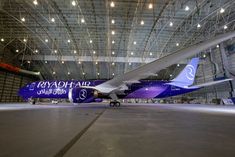 a blue and white airplane parked in a hanger with lights on it's ceiling