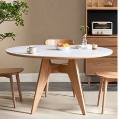 a white table with two wooden chairs and a potted plant in the corner next to it