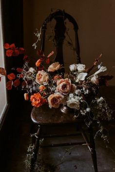 an arrangement of flowers sitting on top of a wooden chair in front of a window