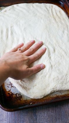 a person's hand on top of dough in a pan