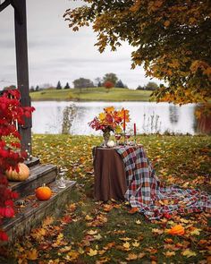 a table with flowers and candles on it in front of a lake surrounded by fall leaves