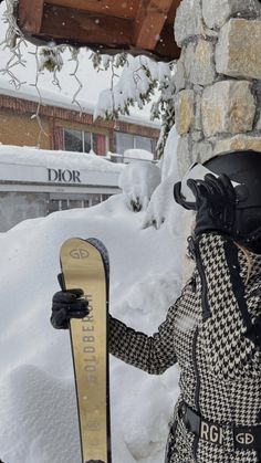 a woman holding a snowboard in front of a stone wall covered in snow with the word dior written on it