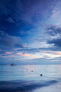 a sailboat floating in the ocean under a blue sky with clouds at sunset or dawn