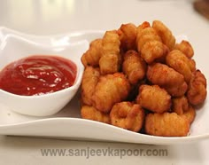 a white plate topped with tater tots next to a bowl of ketchup