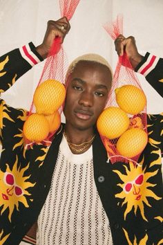 a woman holding oranges in front of her face and wearing a black jacket with sun decorations on it