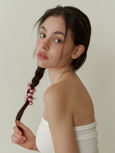 a woman with long hair wearing a white top and holding a pink beaded necklace