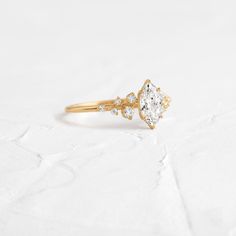 a gold ring with a pear shaped diamond on it's side, sitting on a white surface