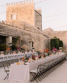 a long table is set up with white linens and flowers for an outdoor dinner