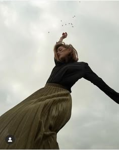 a woman flying a kite in the air with her arms stretched out to catch it