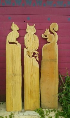 three carved wooden cats standing in front of a red building with purple paint on the wall