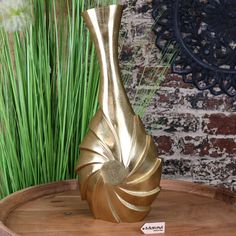 a gold vase sitting on top of a wooden table next to green grass and a brick wall