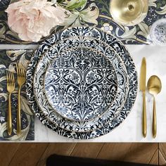 the table is set with black and white plates, silverware, and pink flowers