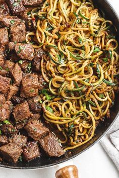 beef and noodles in a skillet on a white surface with chopsticks next to it