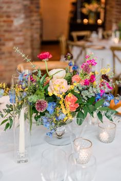 a table topped with vases filled with different types of flowers and greenery next to candles