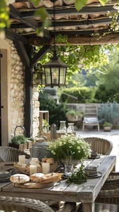 an outdoor dining table and chairs with food on it, under a pergolated roof