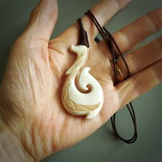 a hand holding a white and brown necklace with a spiral design on it's end