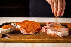 a person is sprinkling seasoning onto some meat on a wooden cutting board