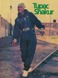 a man in blue jumpsuits standing on train tracks with his hands behind his back