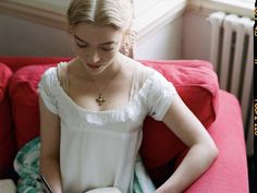 a woman is sitting on a red couch and looking at her cell phone while reading