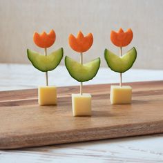 four pieces of fruit with small flowers on them sitting on a cutting board next to cheese cubes