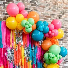 colorful balloons and streamers hanging from a brick wall