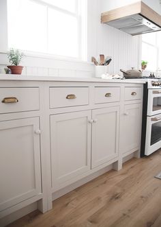 a kitchen with white cabinets and an oven in the center, next to a window that has potted plants on it