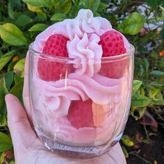 a hand holding a glass bowl filled with strawberries and whipped cream on top of it