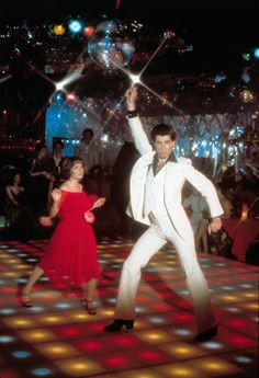 a man and woman dancing on a dance floor with disco balls in the background at a party