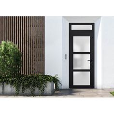 a black and white door sitting next to a planter filled with green plants on the side of a building