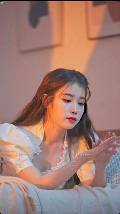 a young woman sitting on top of a bed next to a white wall holding her hands together