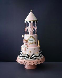 a pink and white carousel cake sitting on top of a wooden table next to a black wall