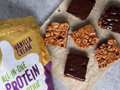 peanut butter and chocolate squares are next to a bag of vanilla cram all - in - one protein bars