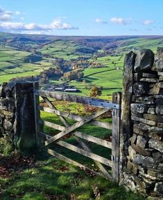 a stone wall and gate in the country side with green fields behind it, on a sunny day