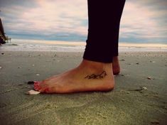 a person standing on the beach with their foot in the sand and mountains behind them