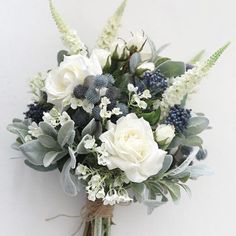 a bridal bouquet with white flowers and greenery on the stems, against a white wall