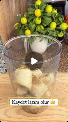 a glass bowl filled with yellow lemons on top of a wooden table next to a potted plant