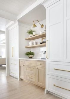 a kitchen with white cabinets and gold handles on the doors, wood flooring and open shelving