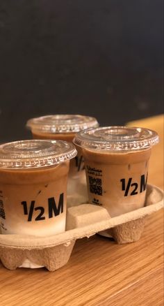 three cups of yogurt sitting in an egg carton on top of a wooden table