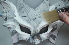 a person holding a paintbrush over a mask made out of newspaper