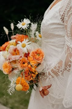 Bride in a lace bell sleeve wedding dress with colourful orange and yellow wedding bouquet Orange Bride Bouquet, Orange Wedding Bouquet Summer, 70s Wedding Flowers, Orange And Yellow Wedding Theme, 70s Wedding Bouquet, Retro Orange Wedding, Orange Flower Bouquet, 70s Inspired Wedding Flowers, Retro Wedding Flowers