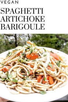 a white plate filled with pasta and vegetables on top of a table next to trees