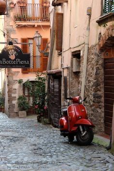 a red scooter parked on the side of a cobblestone street in an old town