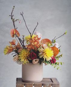 an arrangement of flowers in a white vase on a wooden table with grey wall background