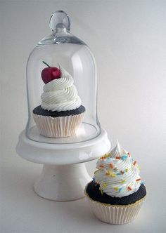 two cupcakes under a glass clochel with white frosting and sprinkles