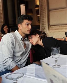 a man and woman sitting at a table with wine glasses in front of their faces