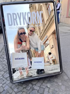 two people are taking a selfie in front of a mirror on the street with their cell phones